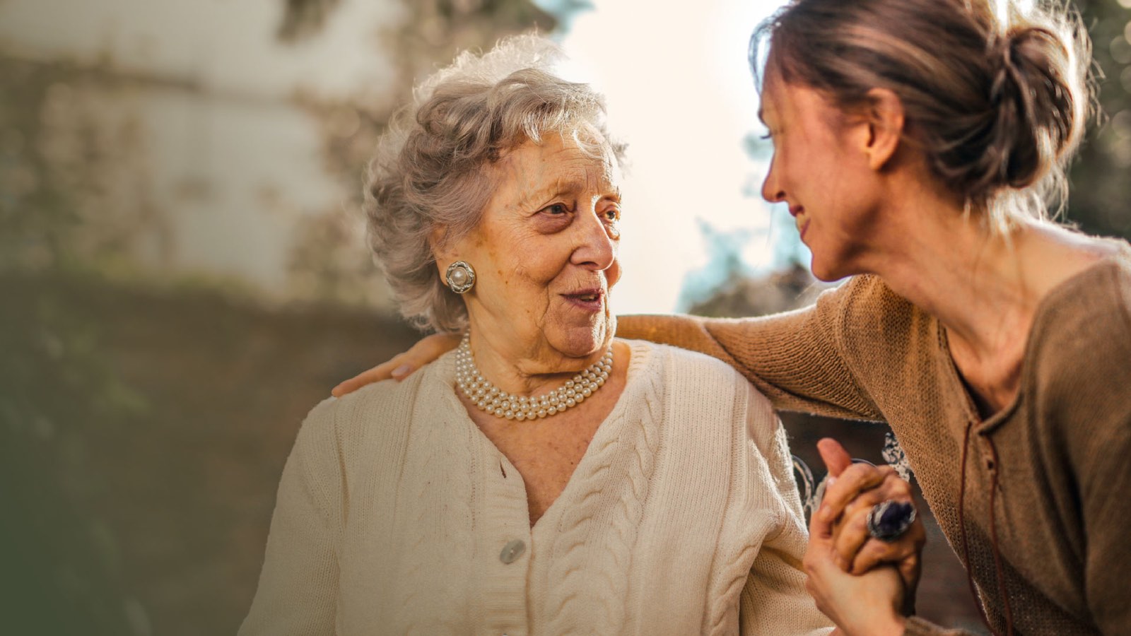 A smiling senior woman holding hands with a younger woman outdoors